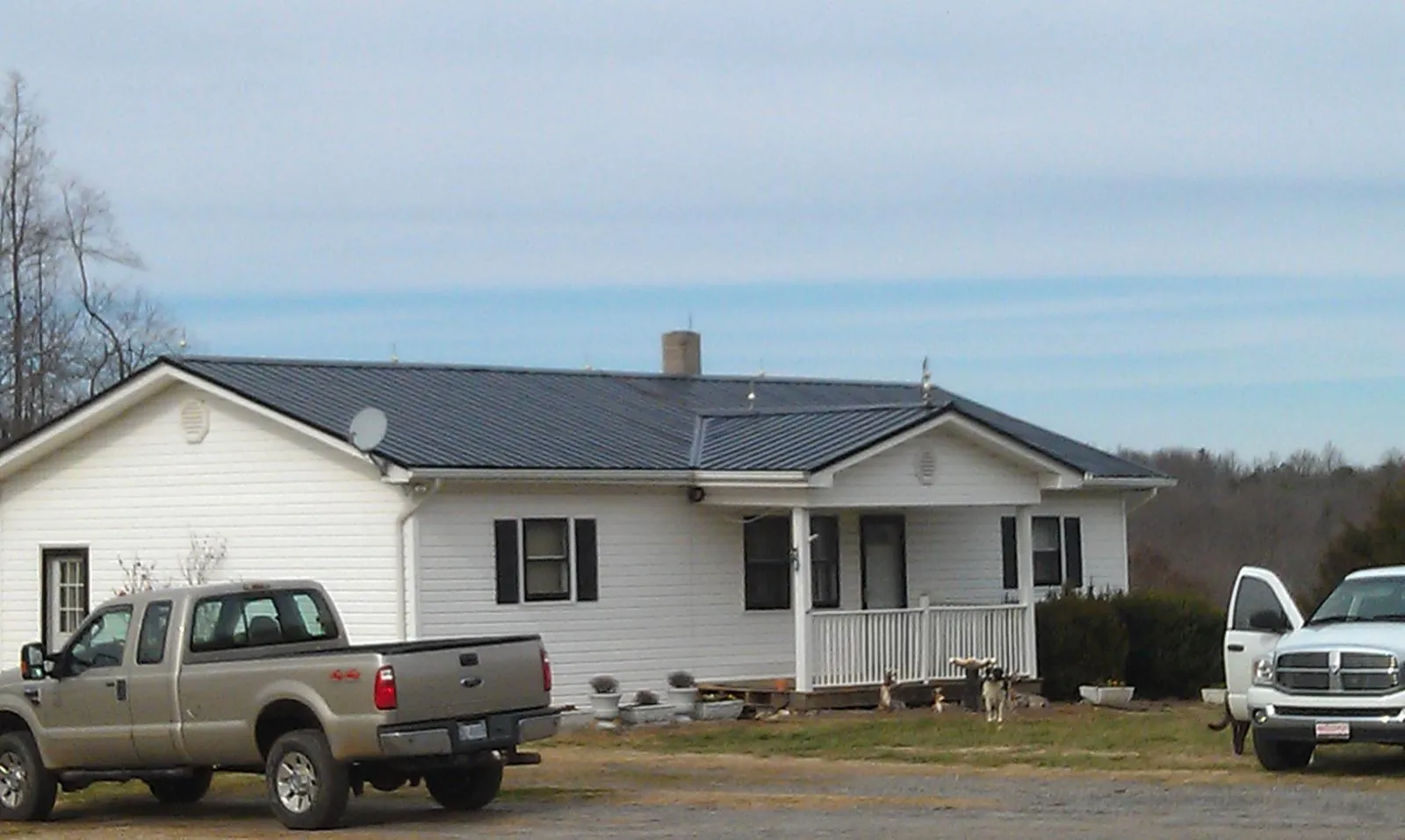 Finished dark metal roof on a white ranch home with work trucks parked in Shelby